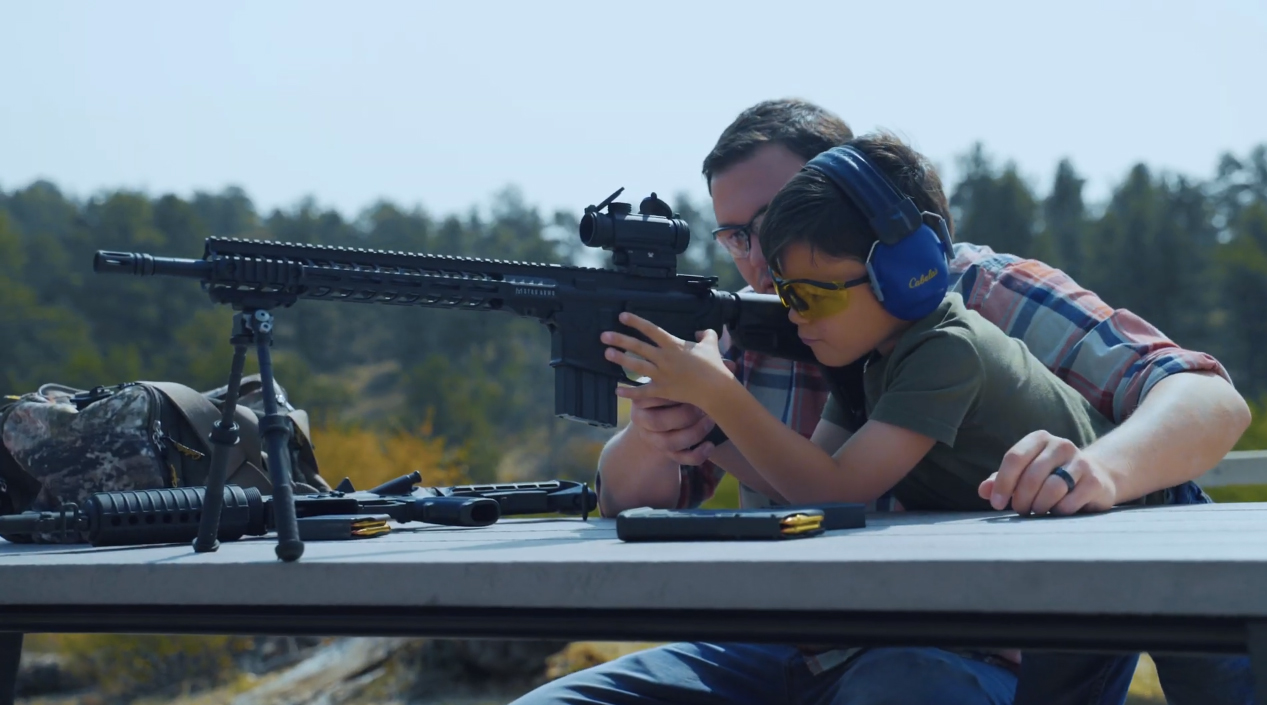 Man teaching kid how to shoot a rifle on a table