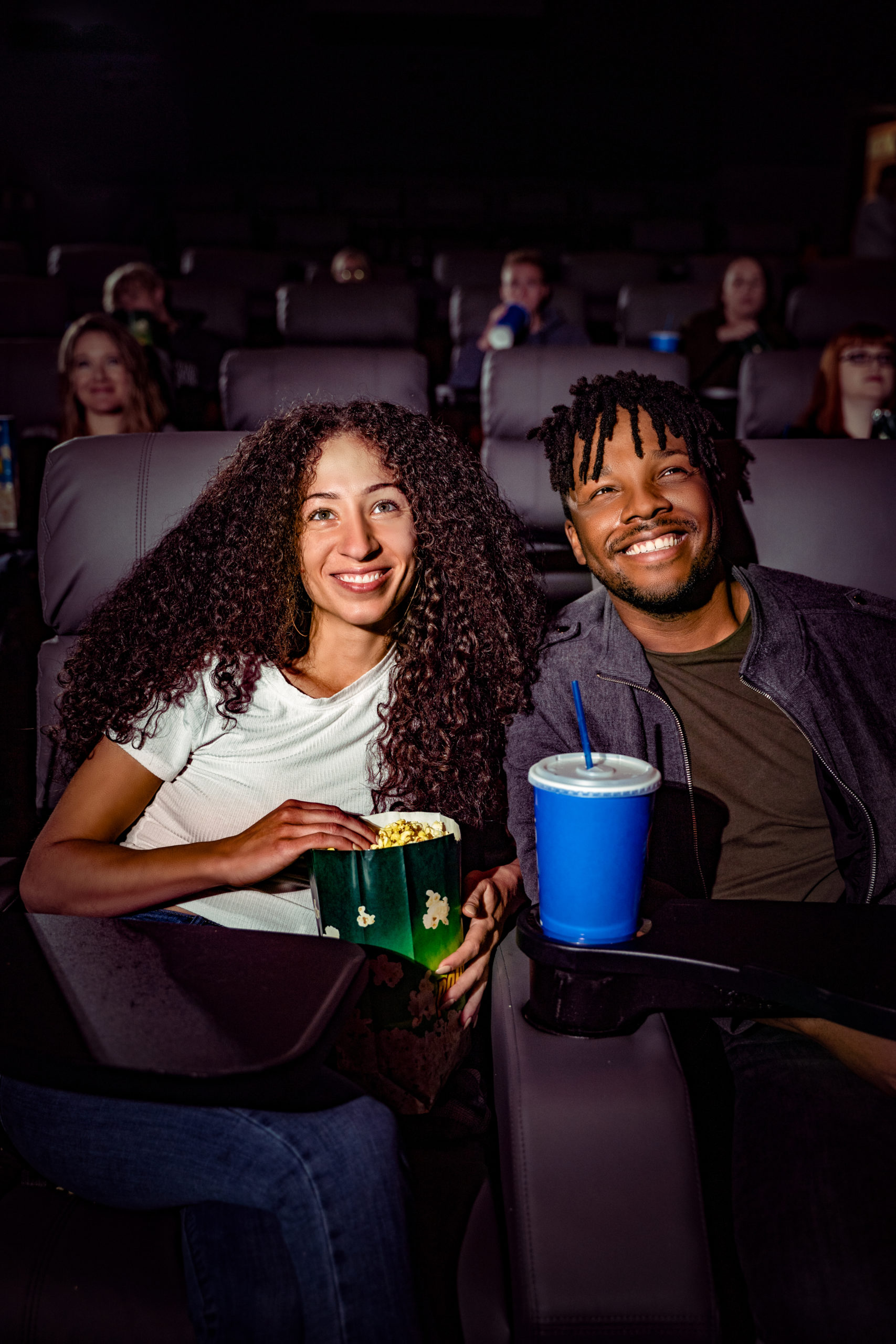 A couple at the movies smiling and eating popcorn